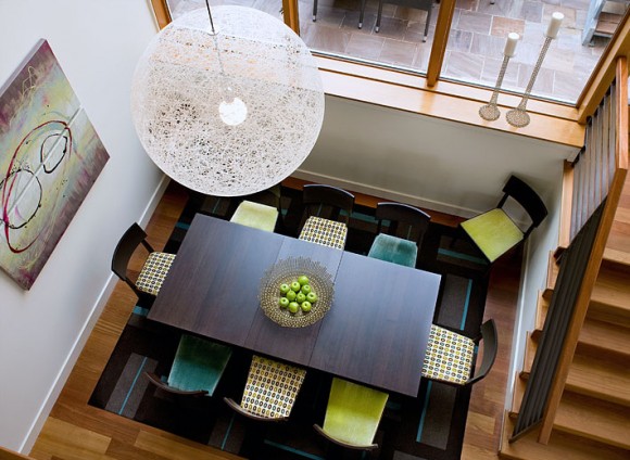 Dining chairs in alternating colors of turquoise, lime green, and spotted patterns surrounding a dark wood dining table, underneath a white globe pendant lamp, as seen from above.