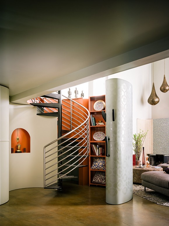 San Francisco loft contemporary circular staircase and custom bookcase that wraps around it in high-gloss orange paint inside the shelving, with white reflective patterned decorated surface facing the living area. An orange display niche on the left white wall matches the orange on the bookcase behind the silver stair railings.