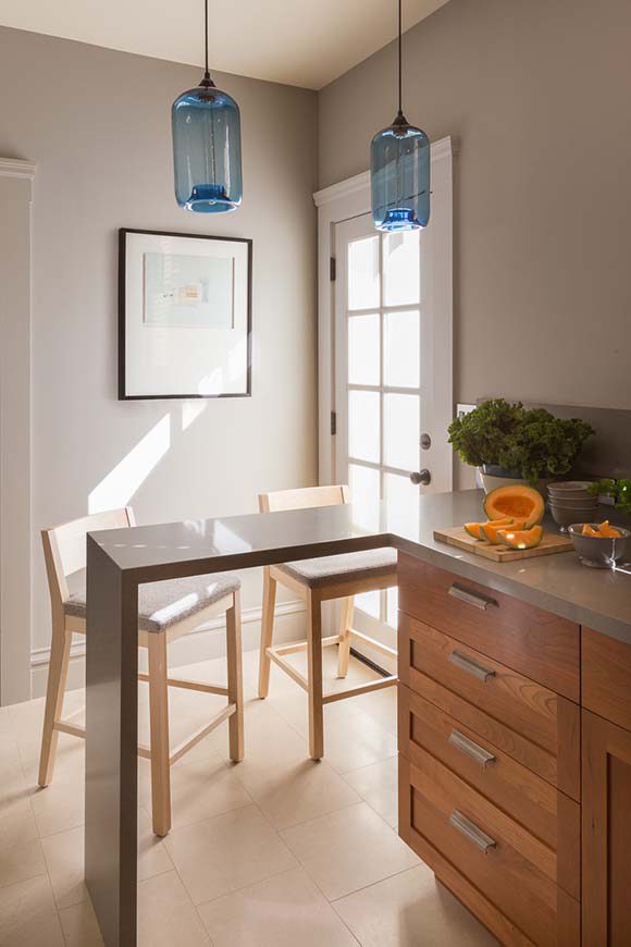 Photo of a kitchen with light streaming in a window next to a breakfast bar with 2 modern stools underneath and artwork on the wall behind.
