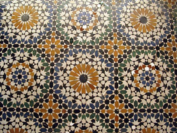 Closeup of intricate geometric tiling pattern in multiple tessellations featuring tiles in white, yellow, black, and blue.