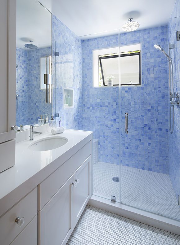 View into a bathroom, with white countertop and sink, white painted cabinetry, white penny tile flooring, and bright blue multicolored mosaic wall tiles, lights either side of the mirror like the master bath in same house, the same operable window as the master bathroom in other photos, and the same showerheads as master bath.