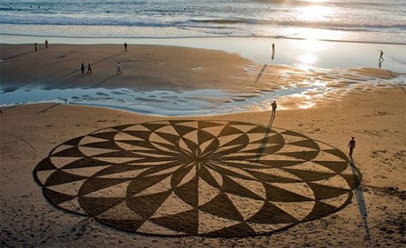 A geometric shape at enormous scale is formed on the beach using only brushes on sand by Artist Andres Amador and his workshoppers.