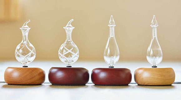 Close-up photo of four nebulizing essential oil diffusers for aromatherapy, shown in three different plantation hardwood base colors and two different delicately hand-blown Pyrex glass patterns, which allow the aroma of pure essential oils to circulate without requiring any heat or water.