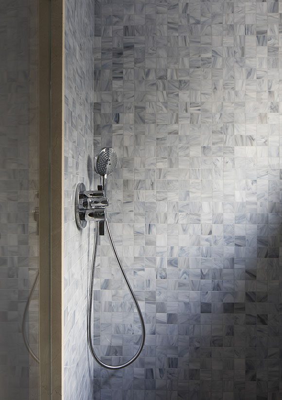 An elegant silver finish hand-held showerhead tones beautifully with the foggy blue-grey multicolored mosaic tiles in this Bay Area-inspired contemporary adult bathroom.