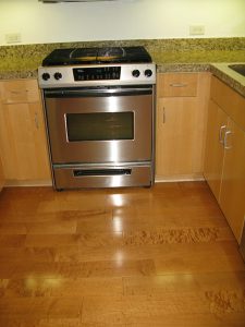 In this homeowner’s own before photo, shades of orangey finishes on the cabinets and flooring don’t tone with each other, and the undercabinet lighting gives off a sickening greenish effect on the countertops.