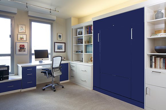 "After” view of the home office, showing the navy blue custom cabinetry that hides the convertible wall-bed and desk, with lovely artwork and neatly organized shelves for storage.