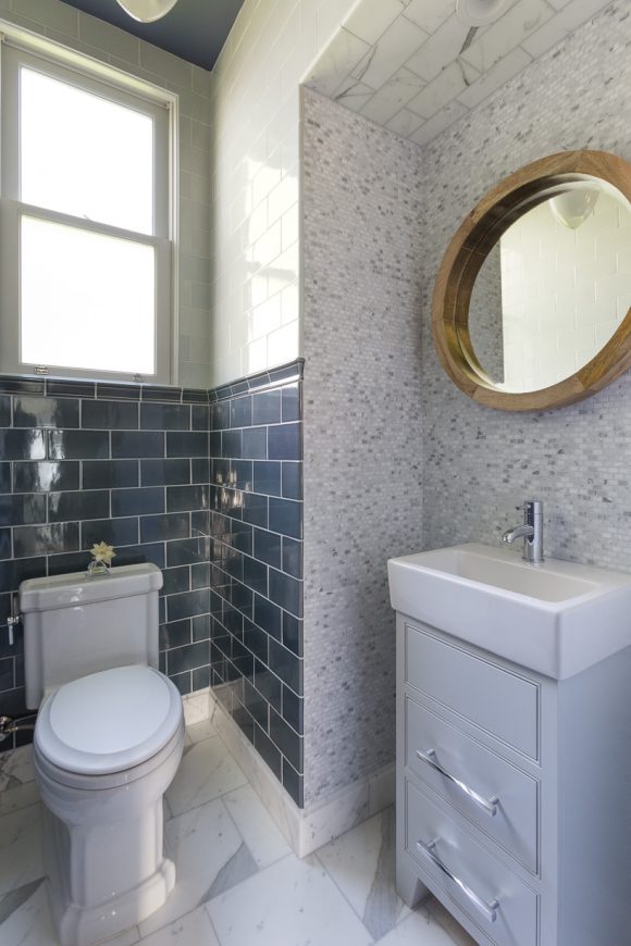 Kimball Starr redesigns this San Francisco powder room with classic white marble and blue subway tiles, plus a round mirror over the white sink basin with storage drawers underneath.