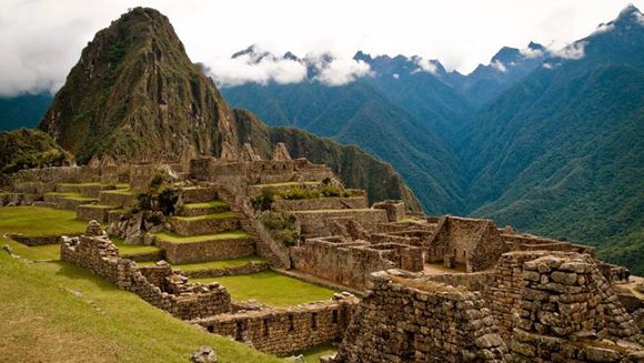 Photo of ancient Incan site Machu Picchu in the cloud-covered green mountains of Peru, with partial stone walls and stairs.