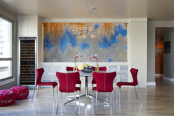 Wine chiller sunken into the wall at left, pedestal table and chairs in front of a colorful painting