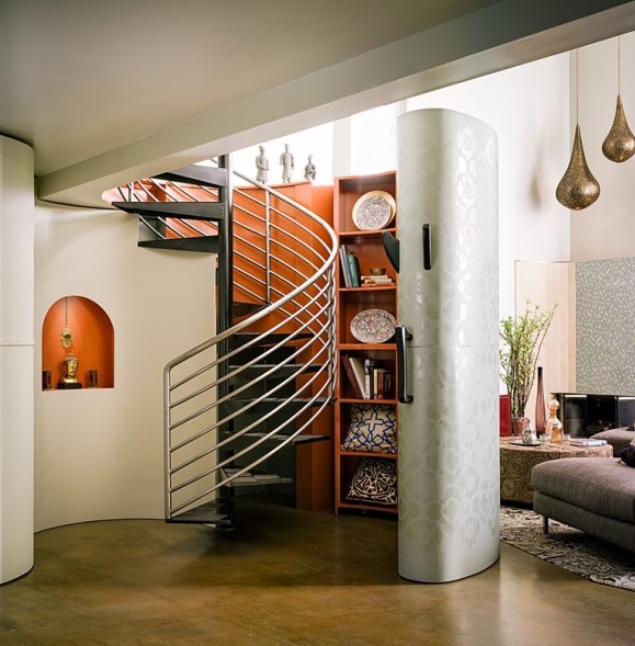 Metal circular staircase with silver railings is complemented by an orange-backed bookcase that twists around the stairs, and can be hidden by a moveable white wall.