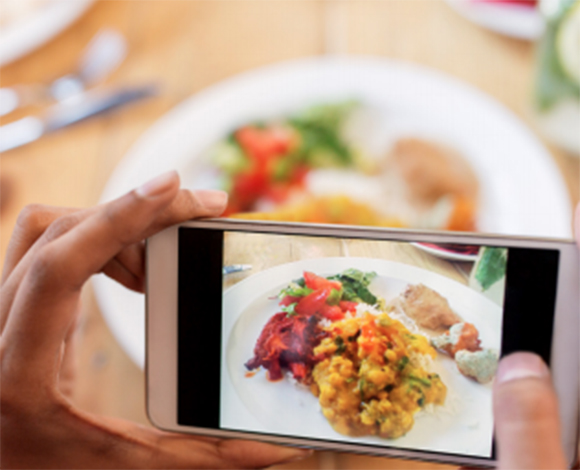Image of a person's handing taking a photo with their cell phone of a delicious meal on a plate.