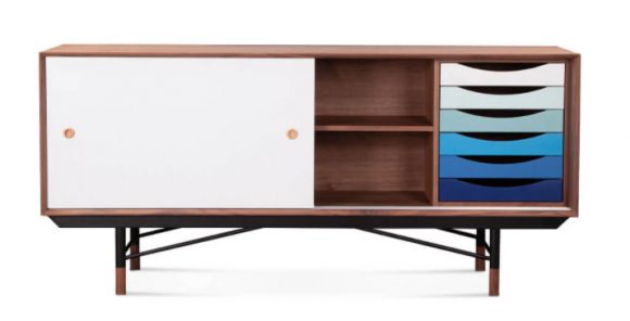 Photo of a sleek modern wood sideboard with a sliding white front door that reveals a set of 6 simple drawers in multiple colors of blue that start light in color and get darker as you go down. The legs are also simple wood with a metal finish.