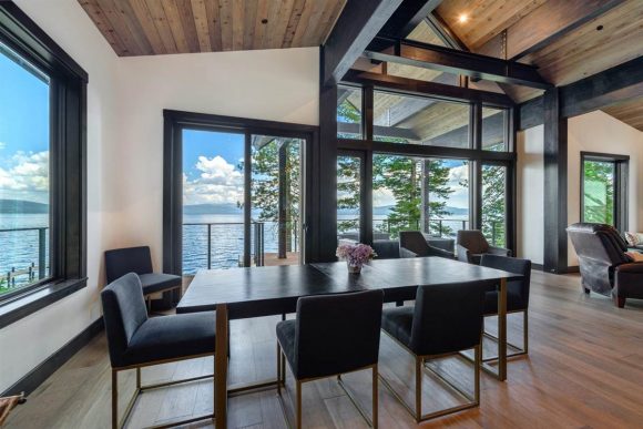 A wooden floor and ceiling, contrasting white walls with windows picked out in black, and a contemporary dining table with seating for 6 all draw your eye out floor-to-ceiling windows to the view at Lake Tahoe.