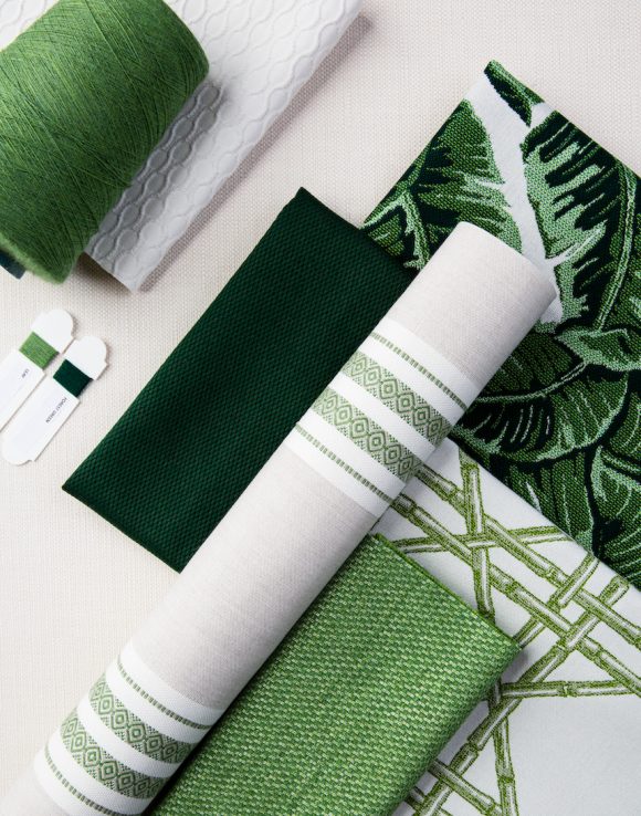 Multiple patterns and types of fabrics in shades of green and white, plus a spool of wool thread, are overlaid in display, showing how they tone together.
