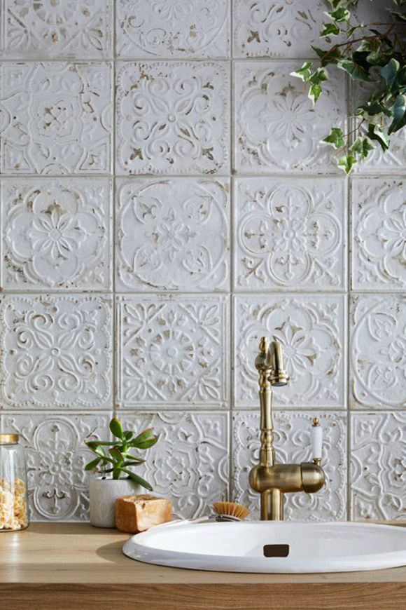 Painted white tiling has some of the paint rubbed off on the raise pattern, exposing the tin color beneath. A brass "victorian" style faucet with a single white ceramic handle completes the space.
