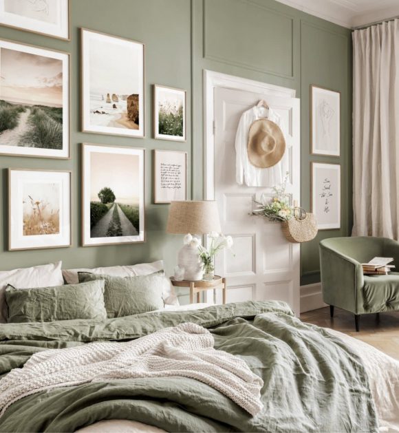 Moss green blankets and white sheets are rumpled on the bed in the foreground. On the moss green walls, paintings and photographs are neatly framed. A white door counterpoints the green. Fresh flowers on the nightstand completes the look.