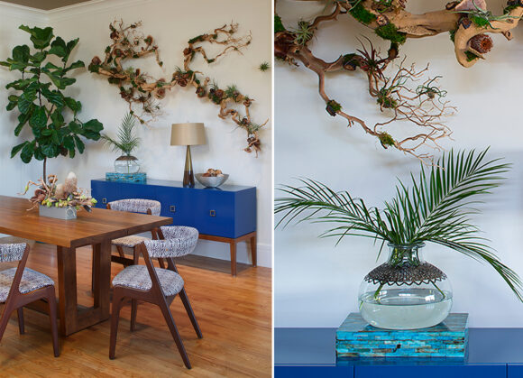 A pair of images of a midcentury-inspired living and dining room space. On the left, medium wood table and chairs with fabric in black and white geometric shapes sit in front of a bright blue sideboard unit. Above the sideboard is a natural wood wall sculpture and to the left is a tall fiddle plant. In the right image, a closeup of a piece of the wall sculpture, and a small live plant clipping in a vase with clear water sits atop a small stack of books on top of the bright blue sideboard.