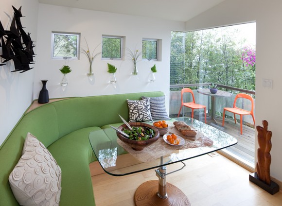 Curved banquette contains storage underneath and is upholstered in outdoor fabric for durability. Adjustable height table is used as a coffee and dining table in this small space.