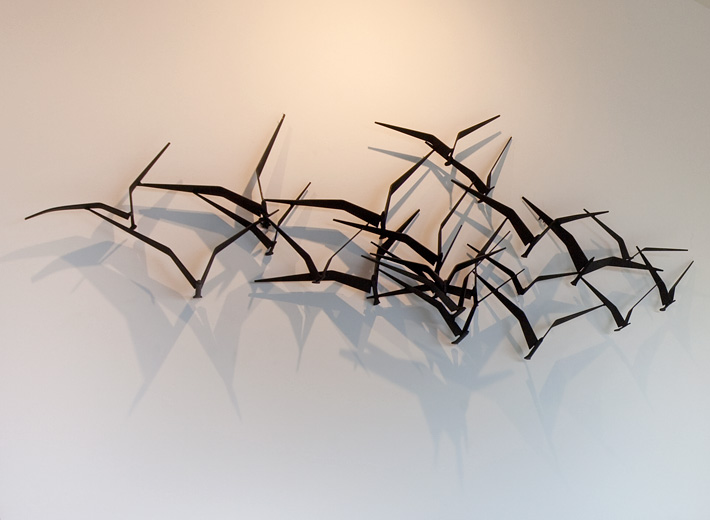 C. Jere iron wall sculpture is made from iron and casts a dramatic shadow of birds in flight.