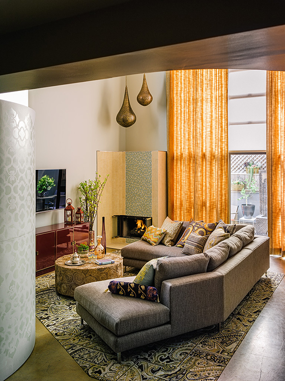 Higher ceiling San Francisco loft living room interior design with tall yellow curtains & patterned rug under an L-shaped sofa in front of flat screen TV
