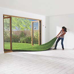 Image of a woman pulling a bright green lawn as if it were a rug into her plain white tiled room