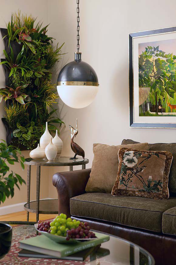 Photo of a corner of a room with a live vertical wall planting, bird sculptures on a side table next to a sofa in leather, with a painting on the wall behind.