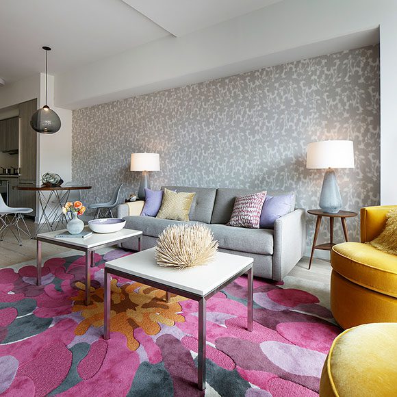 Contemporary San Francisco design firm uses springtime colors to fill the downtown SF Lumina condo with pink and lilac flower rug. yellow velvet swivel chairs, and shadow leaf patterned wallpaper, all designed by award winning design firm Kimball Starr