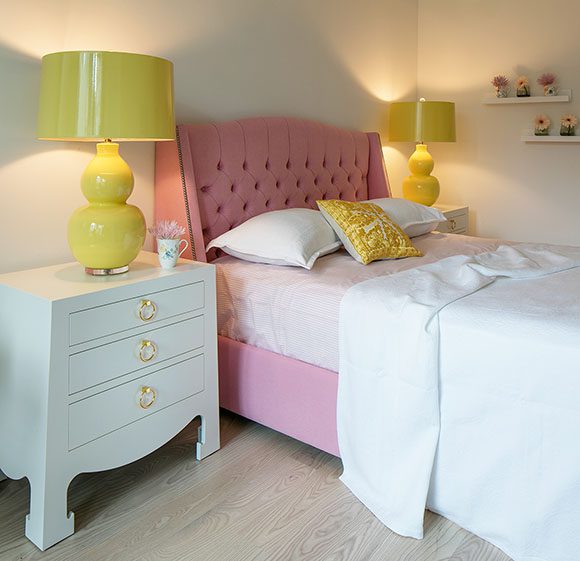 San Francisco decorator creates a feminine bedroom with Bungalow 5 lacquer nightstands and tufted pink bed, and bright yellow glossy lamps.