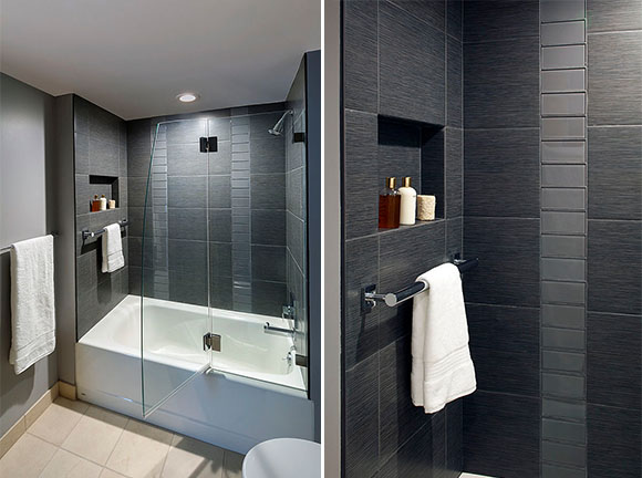 Closeup of an ADA-approved grab bar concealed as a towel rail in a charcoal-grey modern tiled shower and bathroom, below an inset niche for personal products.