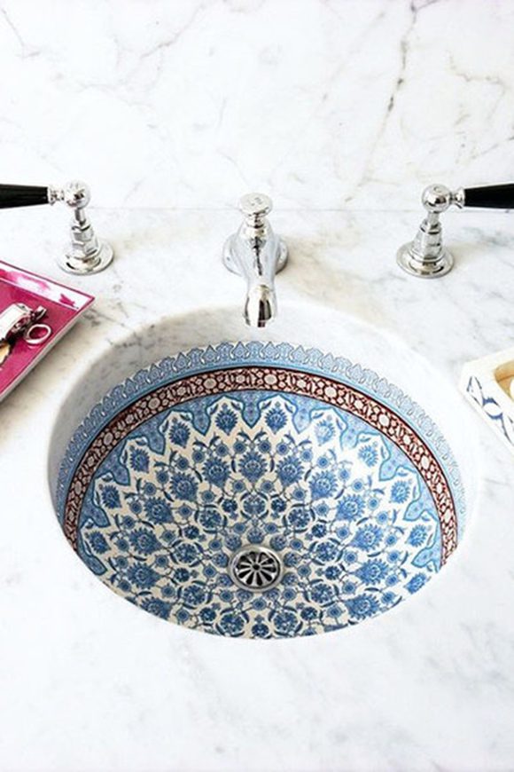 A beautiful round sink basin is tiled inside with intricate floral patterns in blue and white. A delicate copper edging counterpoints the colors almost to the top edge, while simple silver taps and a spigot offer hot and cold water.