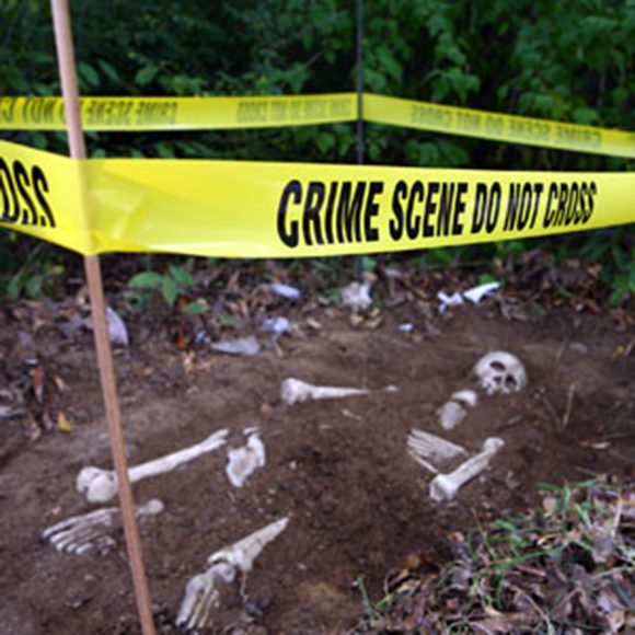 Photo of an area of dirt with a partially-exposed skeleton, surrounded by yellow police "crime scene do not cross" tape
