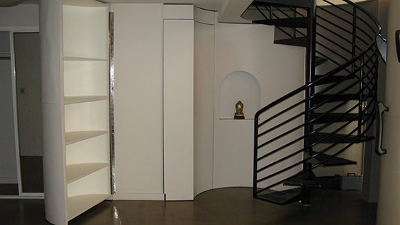 Before the redesign by Kimball Starr, this San Francisco loft had stark white walls and a moveable bookshelf on either side of the black metal circular staircase. A white wall niche holds an urn, but otherwise the space looks unfinished.