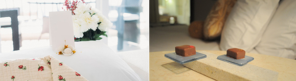 Two images side-by-side. Left showing a white basket of flowers behind the head of a bed, with pink flowered blanket turned down to reveal white sheets, with a white chocolate on the pillow. Right image shows two chocolates on glass trays, next to a pile of pillows on a bed.