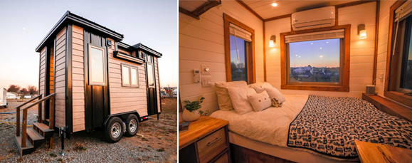 Two photos side-by-side. The left shows the exterior of a tank and dark brown tiny house on a trailer, with three steps off the back. The right image shows the interior with white wooden walls, warm wood trim around the three windows on three walls, and a view of the bed dressed with multiple white pillows, plus a nightstand. The bed has a black-and-white patterned blanket, and two sconces shine warm yellow light down onto the bed. Above the main picture window of the sunset is a split air conditioner/heater.