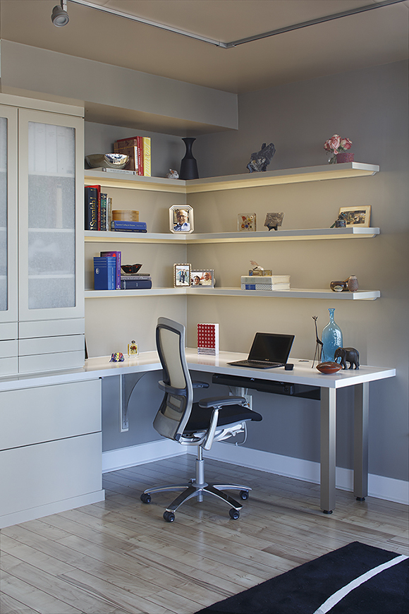 Closer view of the built-in corner desk after the renovation by Kimball Starr. The desk has chunky square silver legs, a white surface that wraps around and joins the built-in drawers and door cabinetry, 