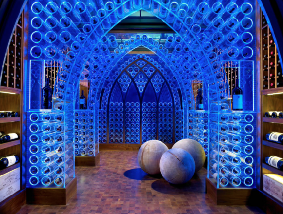 A large wine storage room with lucite plastic storage display that looks like an arched cathedral, all lit up with blue LEDs. On the wooden floor are 3 round balls.