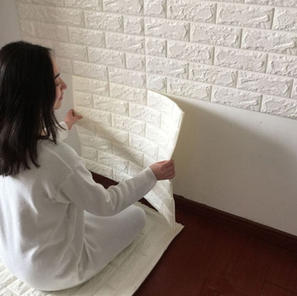 Photo of a woman sitting on the floor, adding vinyl wall coverings of fake white bricks onto her wall.
