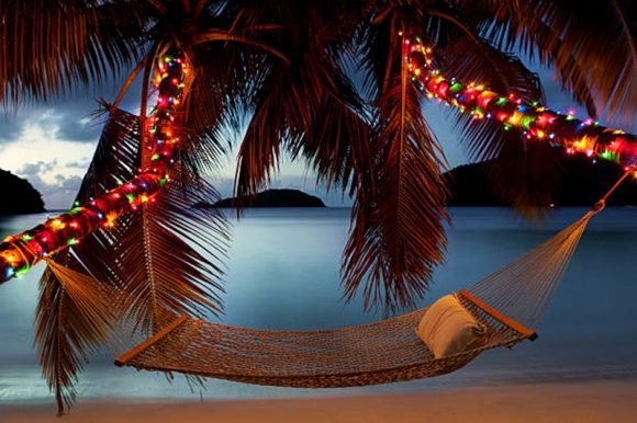Hammock between two palm trees with Christmas lights at a Caribbean beach at sunset - Christmas in the Caribbean