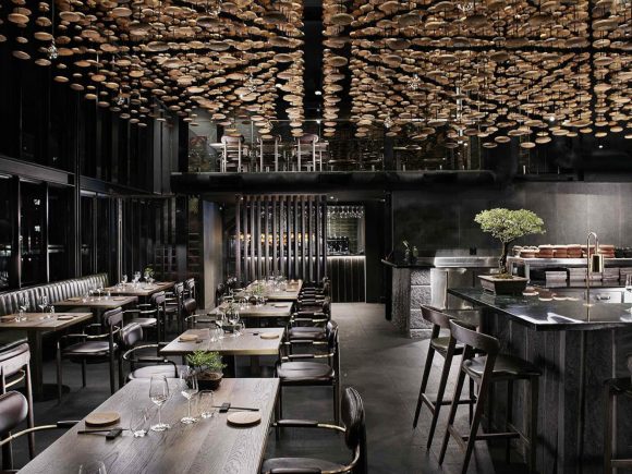 A dark restaurant filled with wooden furniture in the Scandinavian style, with a single bonzai tree on the counter.