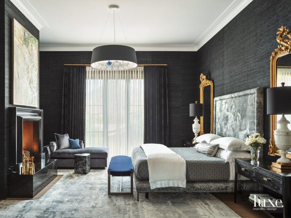 Bedroom featuring black wallpaper, a large black drum pendant light, and a black fireplace opposite a large grey upholstered bed with a Greek scene on the headboard.