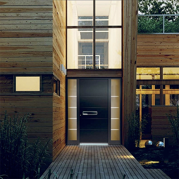 Entrance to a residence with lots of wood cladding in horizontal lines to the left and right of the door and vertical lines on the pathway towards the door. The door itself is black with white sidelight windows either side, and a metal horizontal handle.