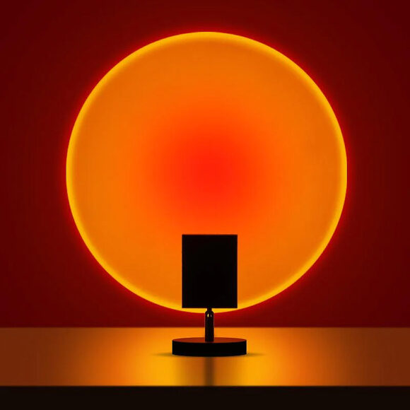 The Sunset table lamp is a small black square on a stand that throws a single large gradiant circle of orange light with red in the center.