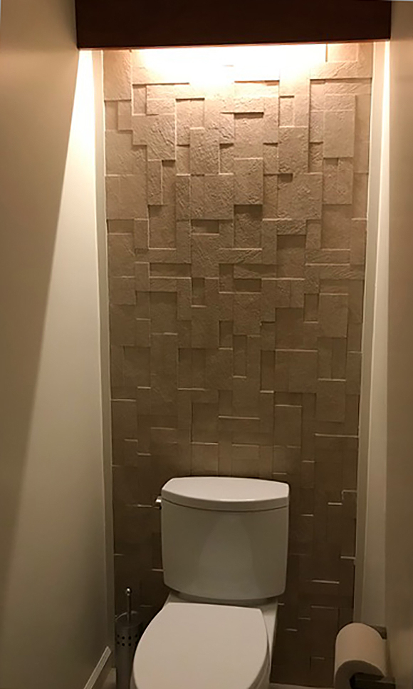 A toilet room has a warm, yellow light coming down from above, across some varied-height raised square tiles, creating shadow and highlights.