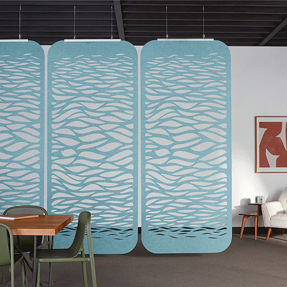 A set of 3 sky blue unconnected hanging screens with wavy-shaped cutouts that get smaller toward the bottom in a room with a set of table and chairs in front of the screens, and an armchair and side table behind, against a white wall. The screens separate the two spaces visually.
