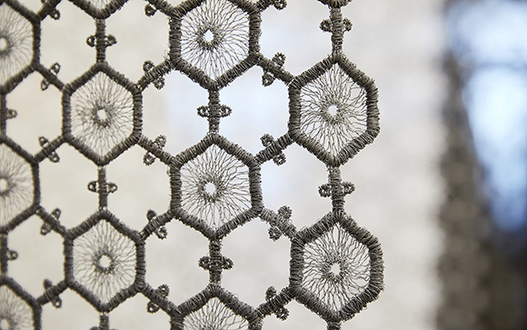 A sound-dampening hanging lace created by embroidered hexagonal shapes filled with thread and connected together, with some hexagons left open.