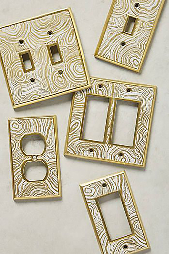 Five different styles of electrical plug plates and light switch plates, all with the same swirled gold and white pattern printed on them, outlined in gold, with drill holes for screws.