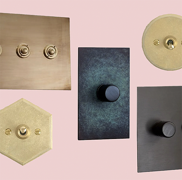Five different metal light switch plates on a pink background. Top left is brass with two round buttons, below that is hexagonal gold with a single switch and two screws, in the center is a dark green and black mottled square plate with a black round knob in the center, top right is a circular gold plate with a switch in the middle and two screws either side, and bottom right is a grey metal rectangular plate with a single grey metal knob in the center.