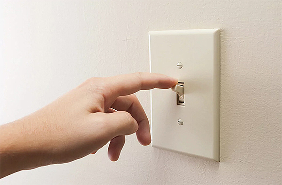 A man's hand with a finger extended to the tip of a standard off-white American-style light switch