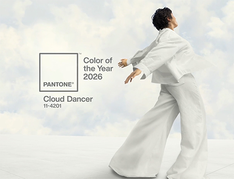 Pantone Color of the Year for 2026 is a fluffy white called Cloud Dancer, illustrated by a woman with short dark hair, back turned to the camera, with her arms behind her as if blowing in the breeze. Her wide pant legs are catching the wind also, and fluffy white clouds surround her against a pale blue sky.