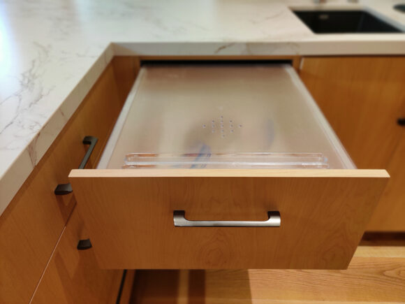 A pull-out bread drawer with a built-in cutting surface keeps bread and pastries fresh. Fronted with the same light oak finish to blend in with the rest of the kitchen.